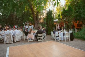 Outdoor wedding reception setup with white chairs and dance floor surrounded by trees.