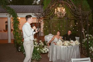 Decorated outdoor wedding reception area with elegant chandeliers and greenery arches.