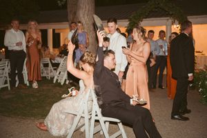 Wedding guests celebrate at an outdoor reception as couple shares special moment on white chairs.