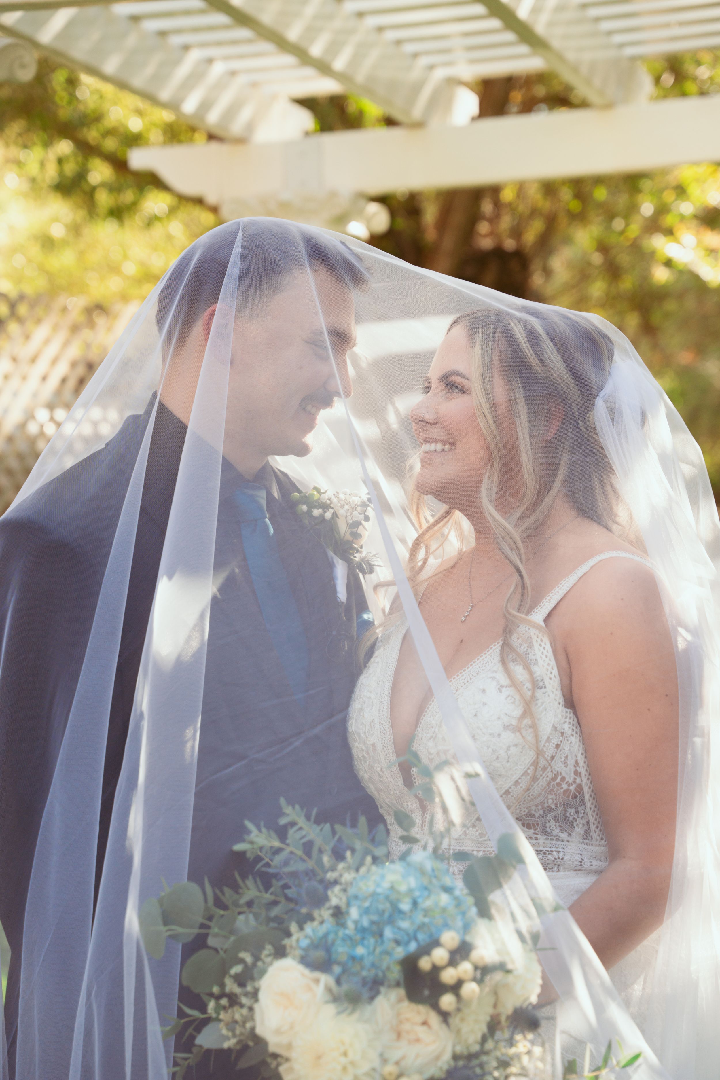 A joyful wedding couple sharing tender moments under a white veil in golden sunlight.