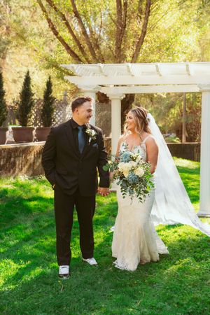 A couple shares a joyful moment under a white pergola on their wedding day surrounded by lush greenery.