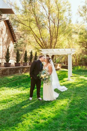 A wedding couple shares intimate moments under a white pergola in a lush garden setting.