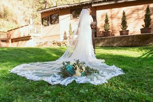 Elegant cathedral veil with floral bouquet spread out on lawn with rustic venue backdrop.