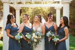 Wedding party of bridesmaids in matching navy dresses share candid moments under white pergola.