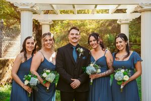 Wedding party wearing navy blue dresses and suits poses together under a white pergola.