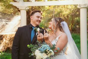 Newlywed couple laugh together under garden pergola with turquoise and white floral bouquet details.