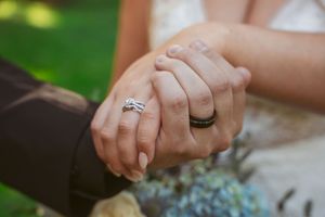 Close-up hands showing off sparkling engagement and wedding rings with a green garden background.