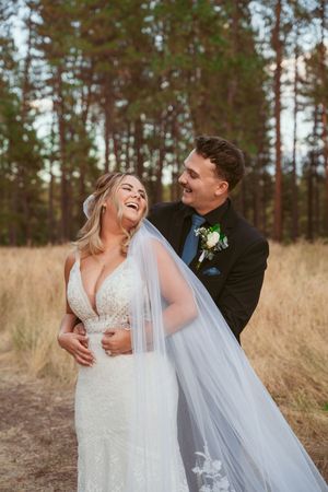 Candid outdoor wedding photos showing playful moments between newlyweds in a field with pine trees.