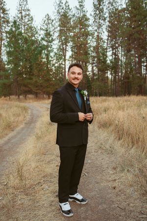 A dirt path winds through tall dried grass and pine trees at golden hour.