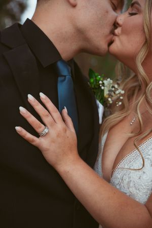 A close-up shot of a romantic kiss showing an engagement ring and formal wedding attire.