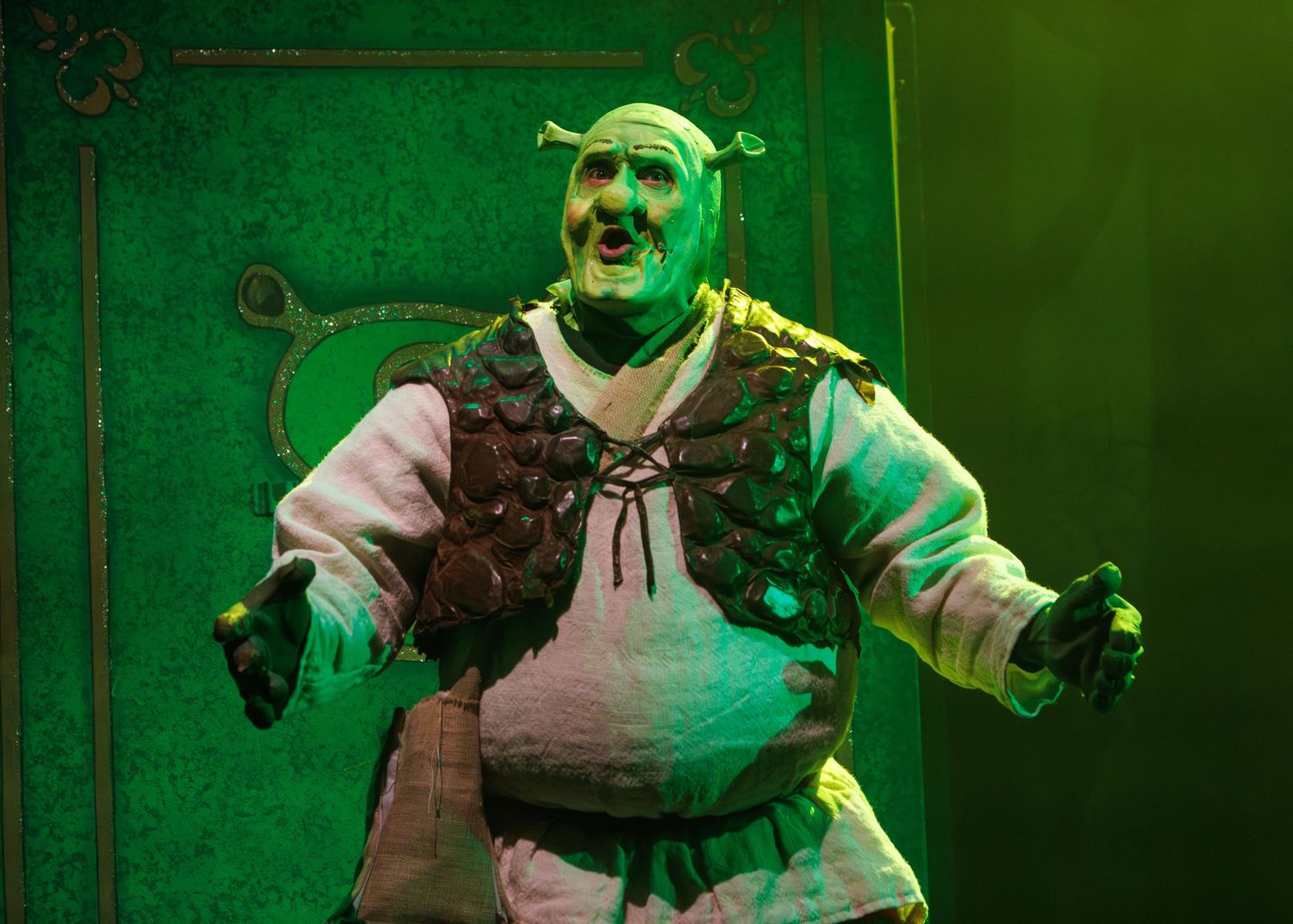 Performer in spooky green lighting moves dramatically across stage during theatrical production.
