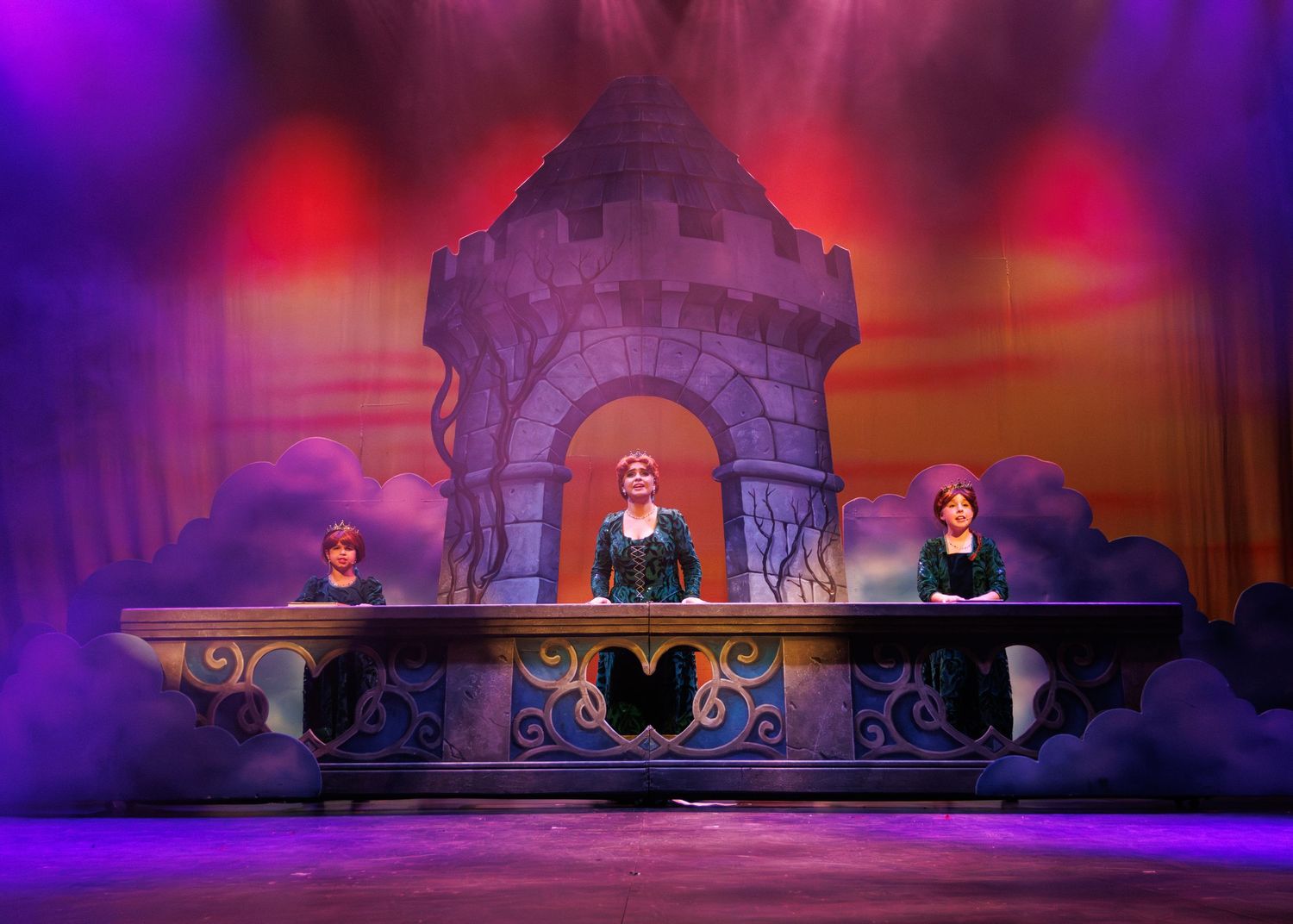 Stage performance scene with three performers on an ornate stone balcony with dramatic purple and red theatrical lighting.