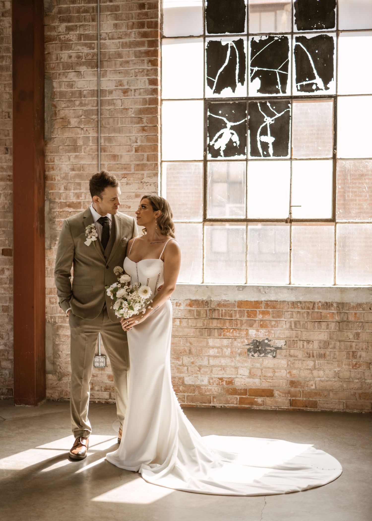 Wedding couple dancing playfully in rustic brick industrial space with natural light.