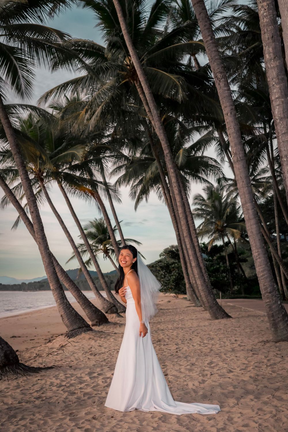 A white flowy dress on a sandy beach with tall palm trees swaying in the tropical sunset light.