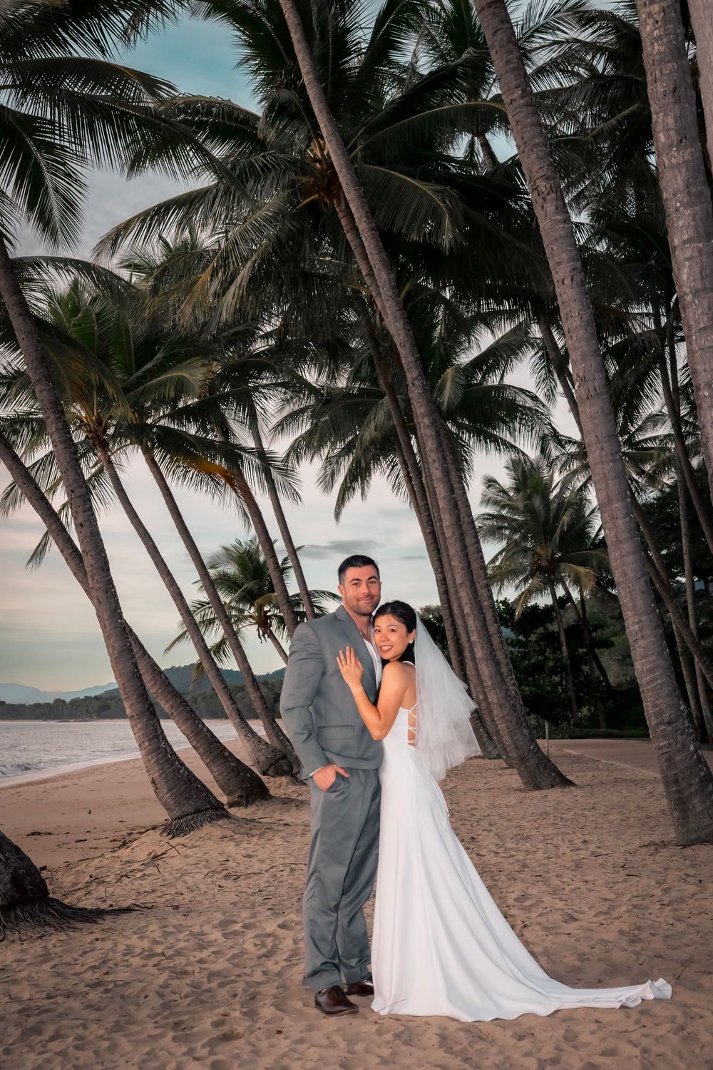 Romantic beach wedding photos at sunset with palm trees swaying in the background on a sandy tropical shore.