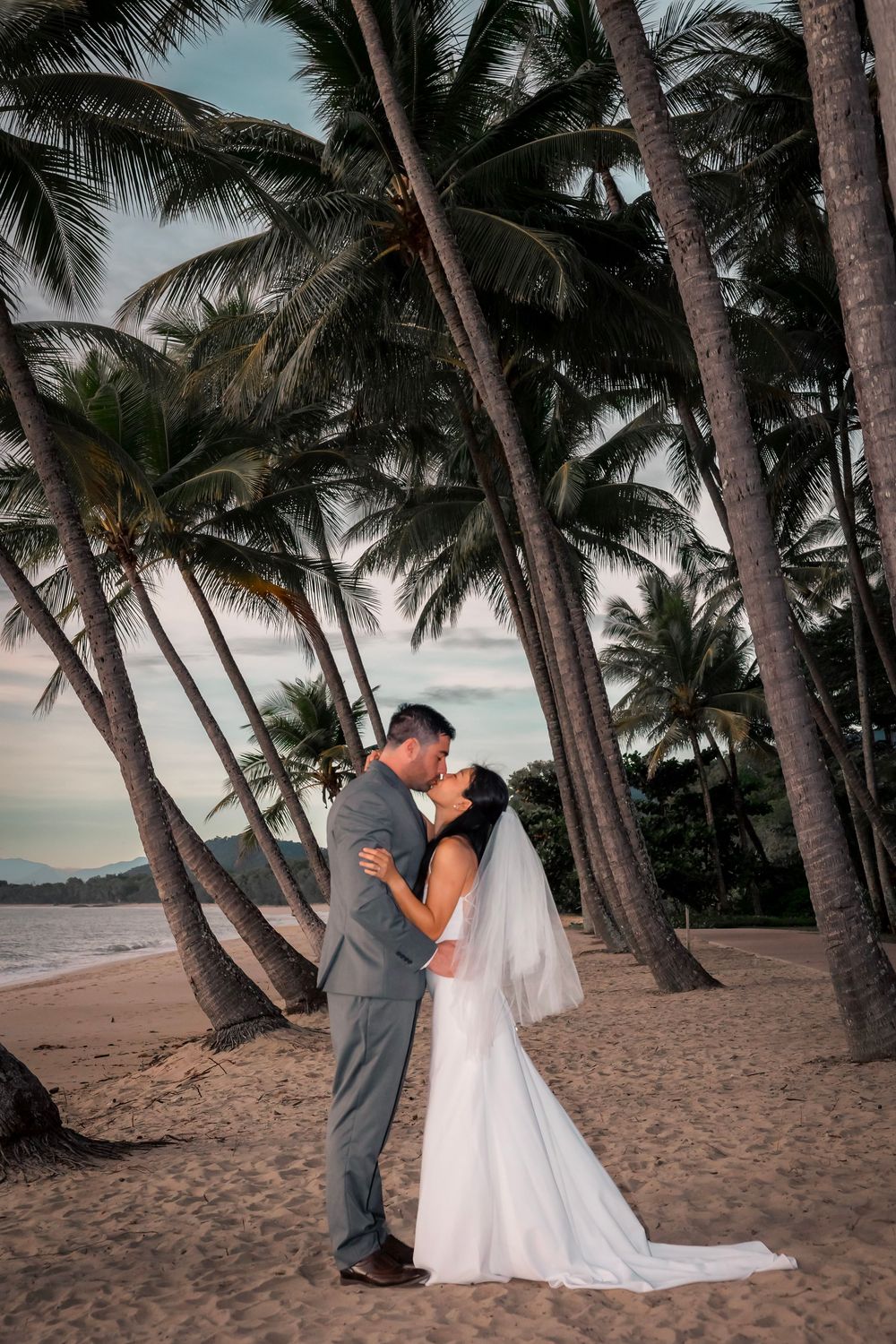 A romantic beach wedding photoshoot series featuring a couple kissing among palm trees at sunset.