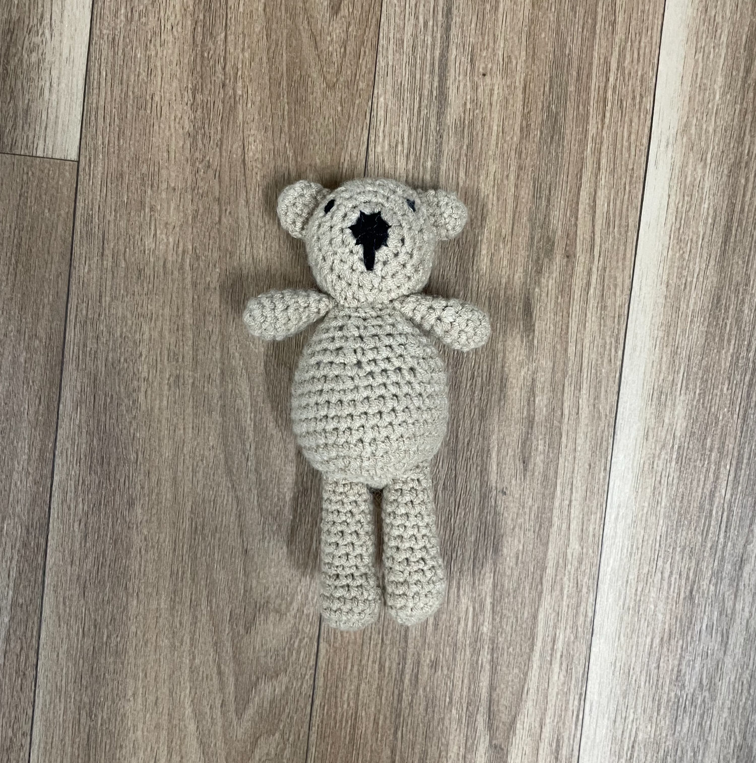 A hand-crocheted white teddy bear plush toy on a wooden floor.