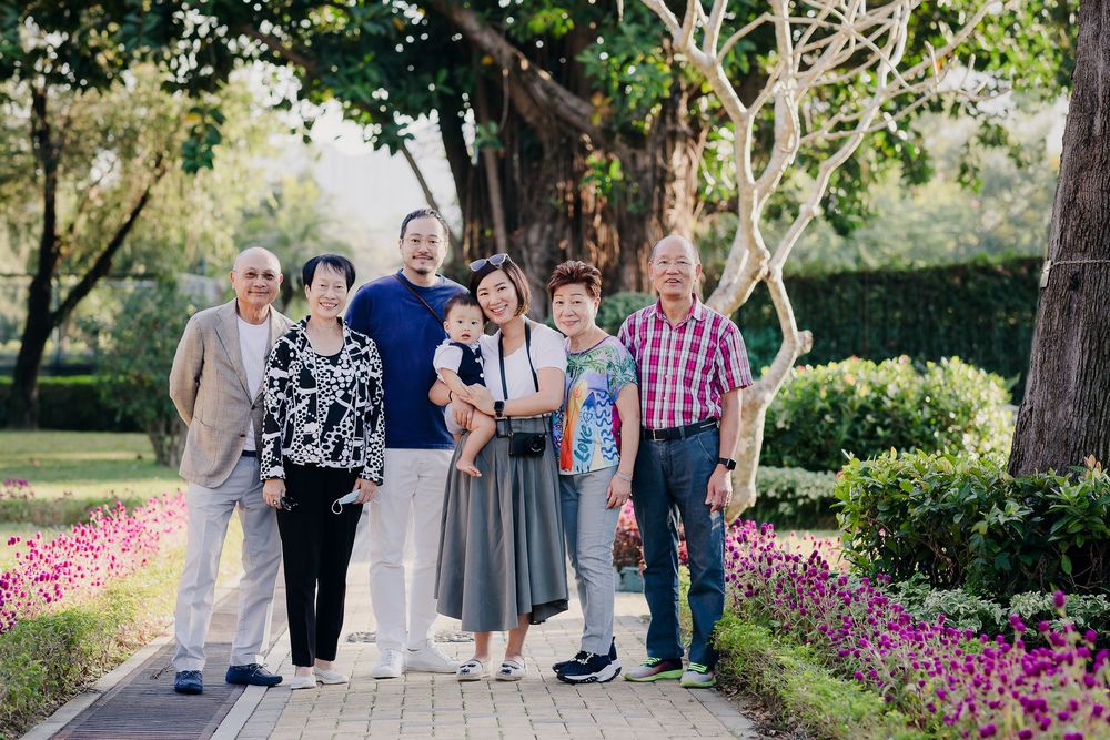 Group of people standing together on a garden path surrounded by blooming pink flowers and lush trees.
