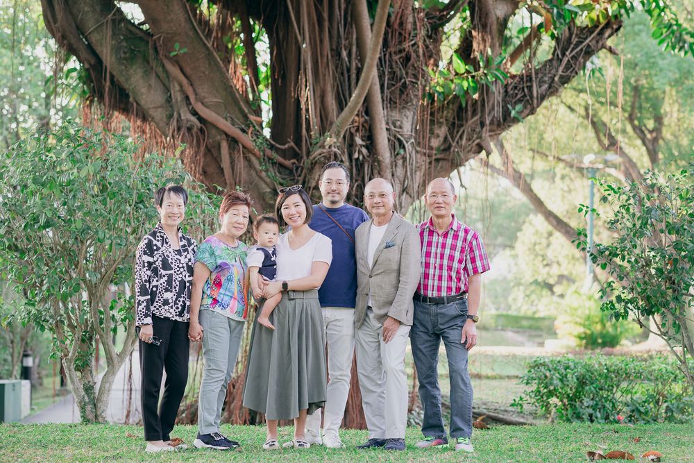Group gathers beneath towering trees in an outdoor setting for casual photo session.