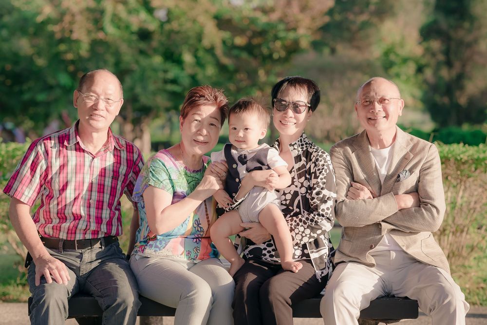 Group of people dressed casually sitting and smiling outdoors in a natural setting during a sunny day.