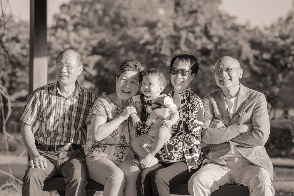 Family members laugh together while sitting outdoors during a cheerful photo session in a natural setting.
