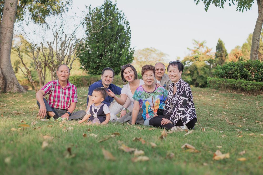 A group of people sitting together outdoors on grass during a warm autumn day for family photos.