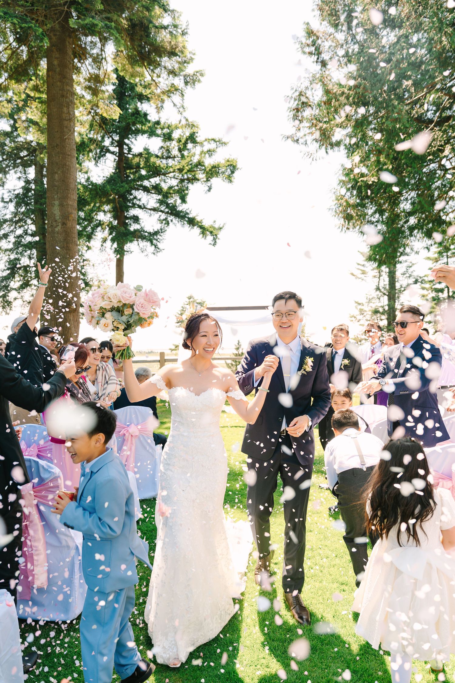 Wedding guests celebrate with confetti and joyful dancing during an outdoor celebration in a sunlit garden setting.