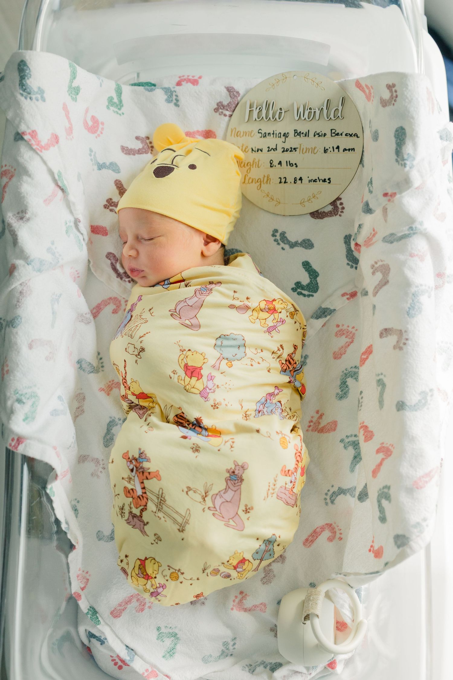 Sleeping newborn baby wrapped in yellow floral swaddle blanket against white background with butterfly pattern.