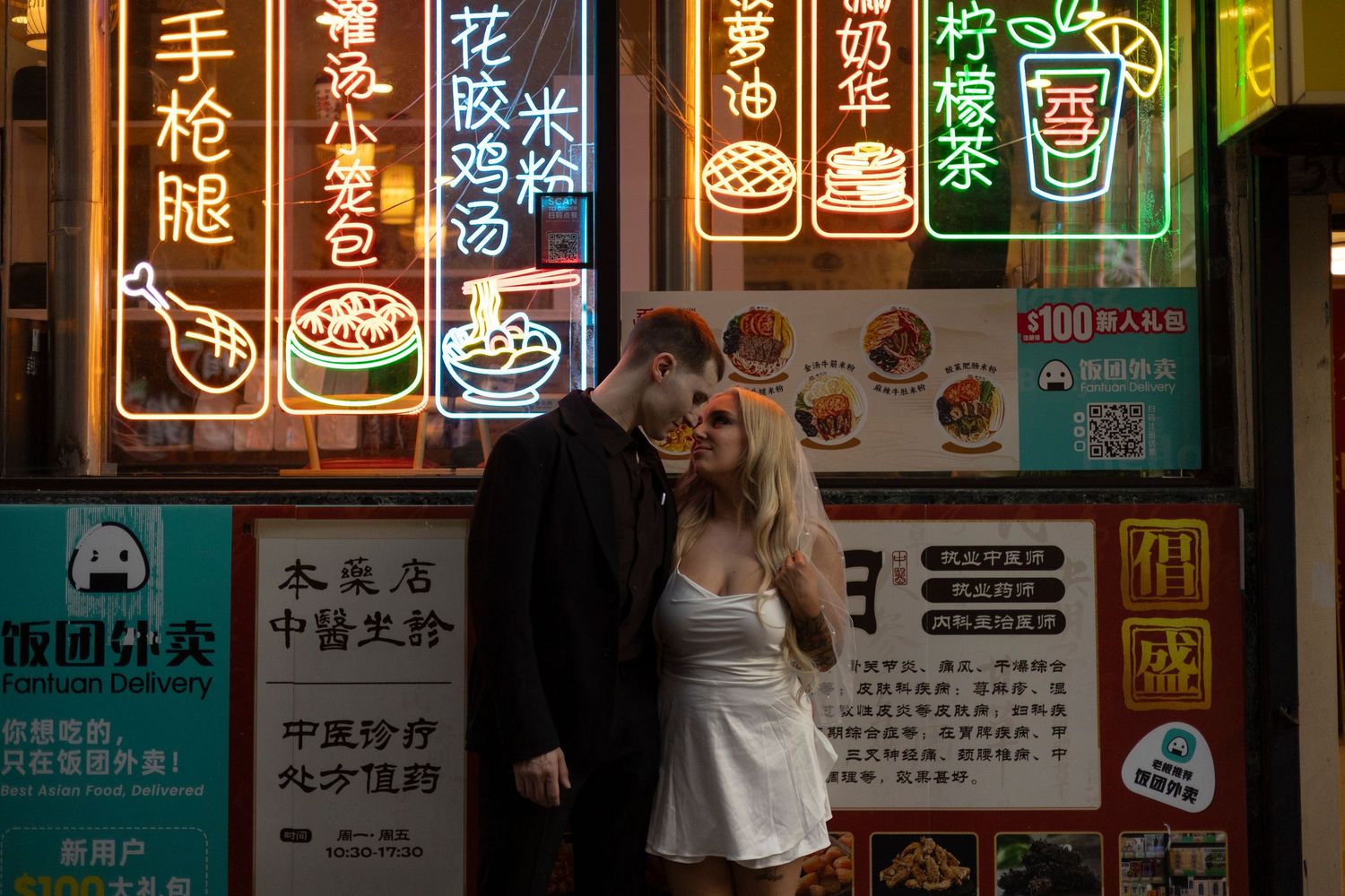 Colorful neon signs and menu boards illuminate a busy street at night in an Asian shopping district.