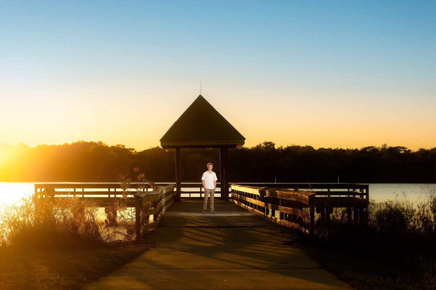 A person stands against a rustic metal gate at sunset in a golden field with warm backlighting.