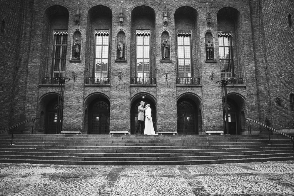 A black and white panoramic collage of a historic brick building with arched windows and stone steps.
