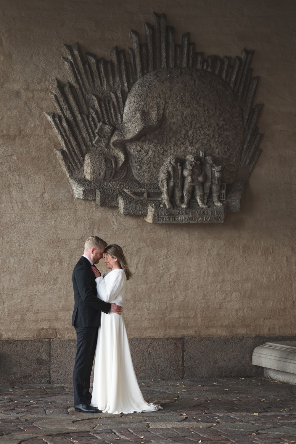 A romantic wedding couple shares intimate moments under an ornate architectural detail in a historic stone building.