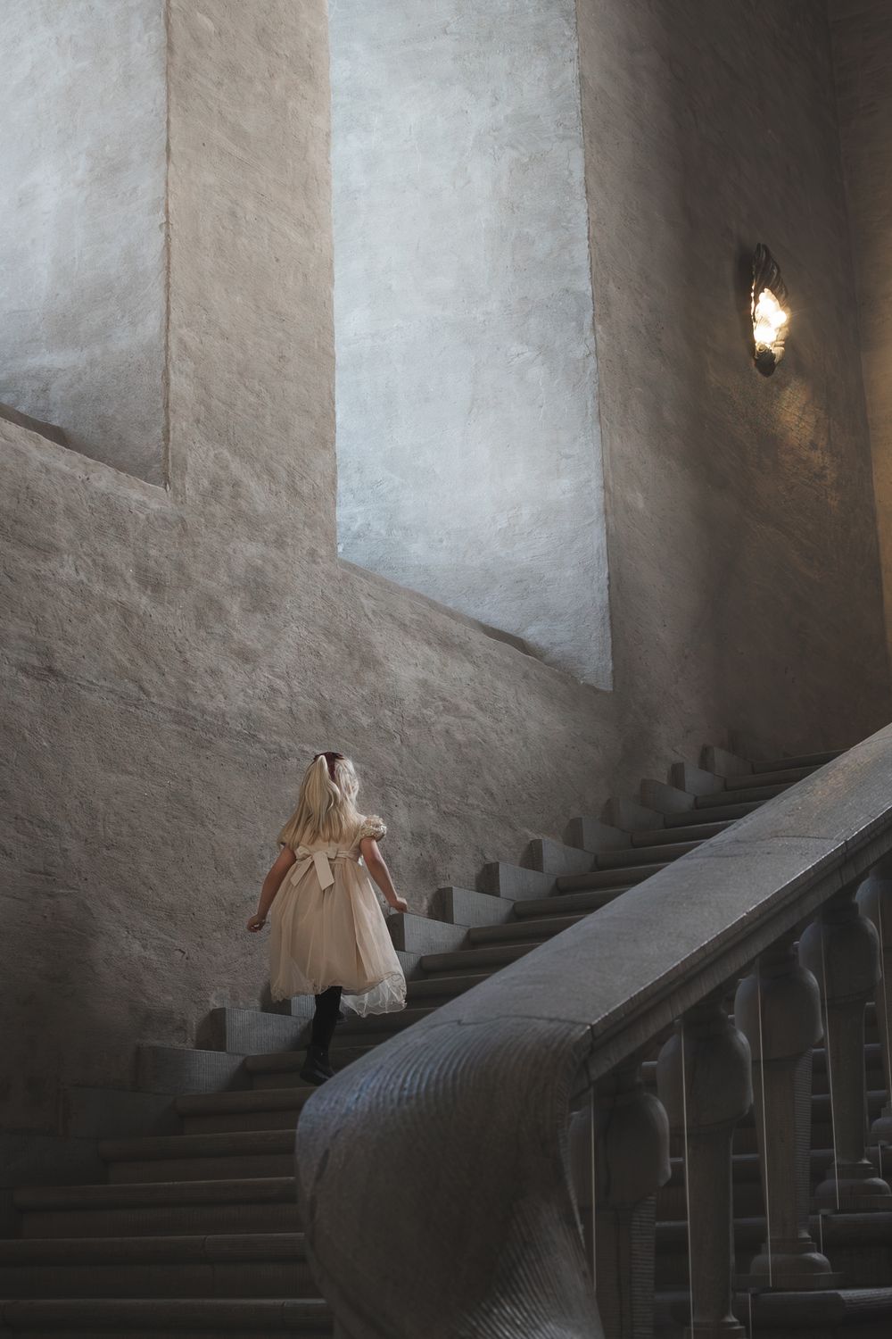 A ghostly figure in a white dress ascends a dimly lit stone staircase in an atmospheric medieval castle interior.