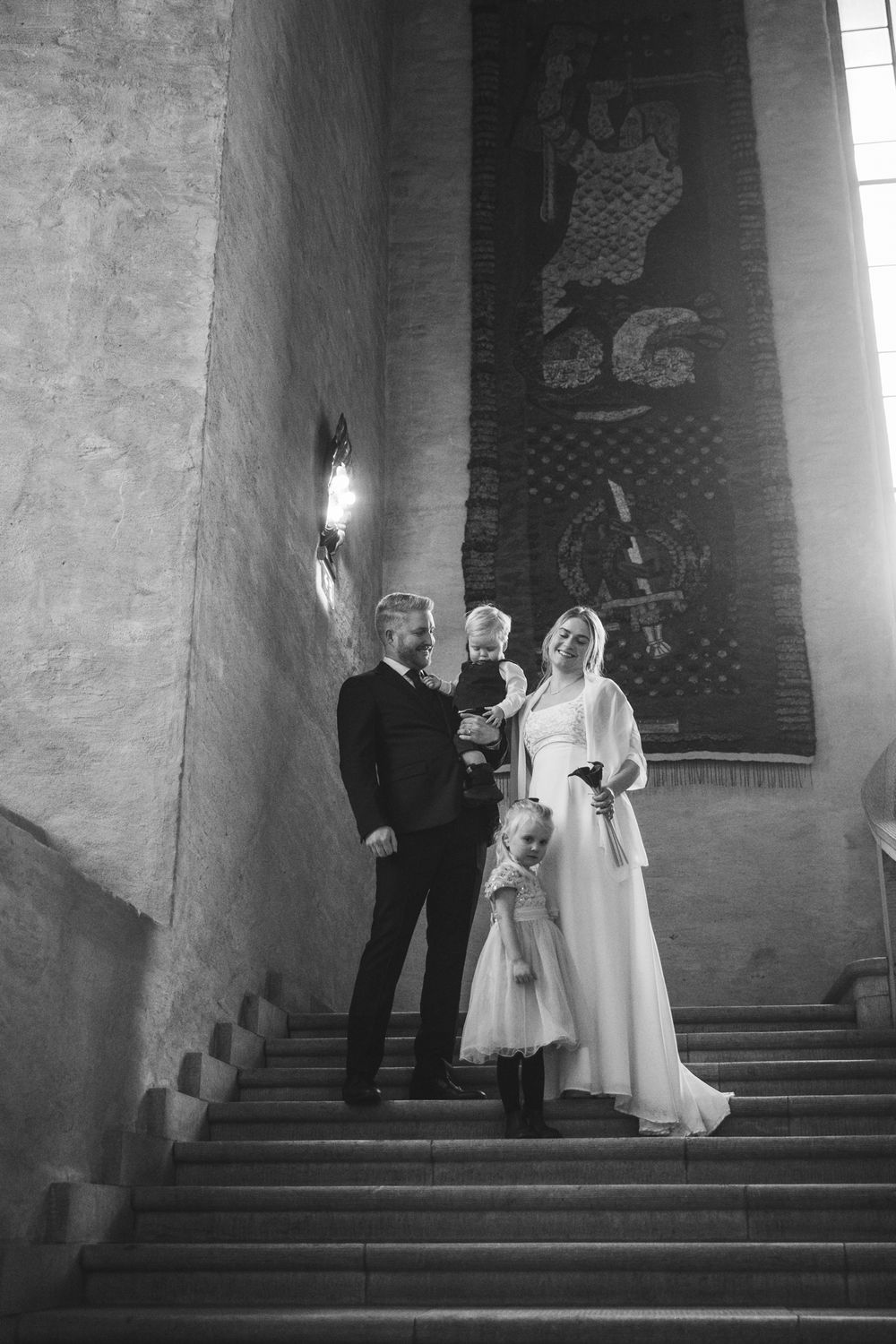A black and white wedding photograph taken on church steps with a tall decorative wall in the background.