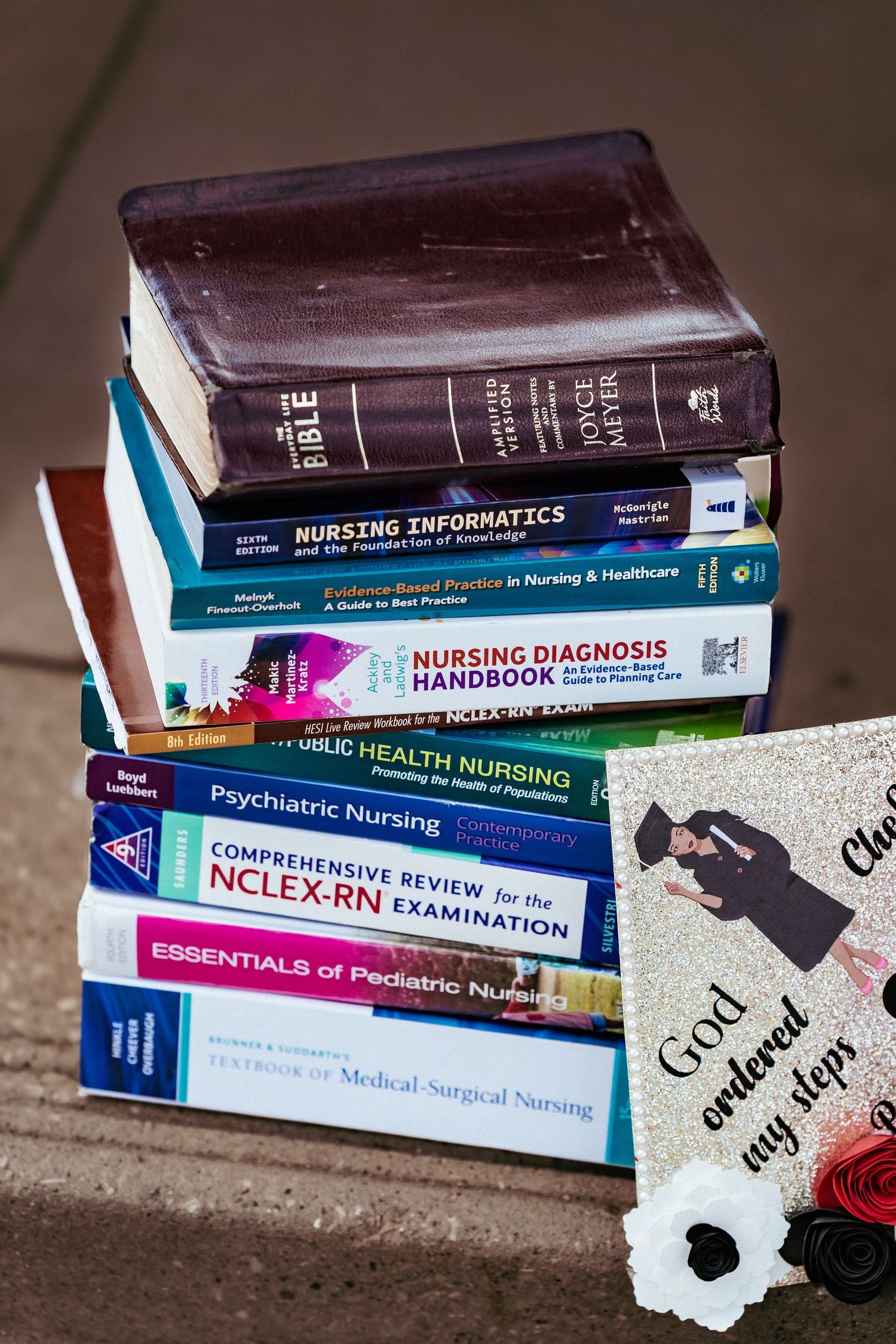 Stack of nursing textbooks and medical reference materials on a dark surface with focus on spines and titles.