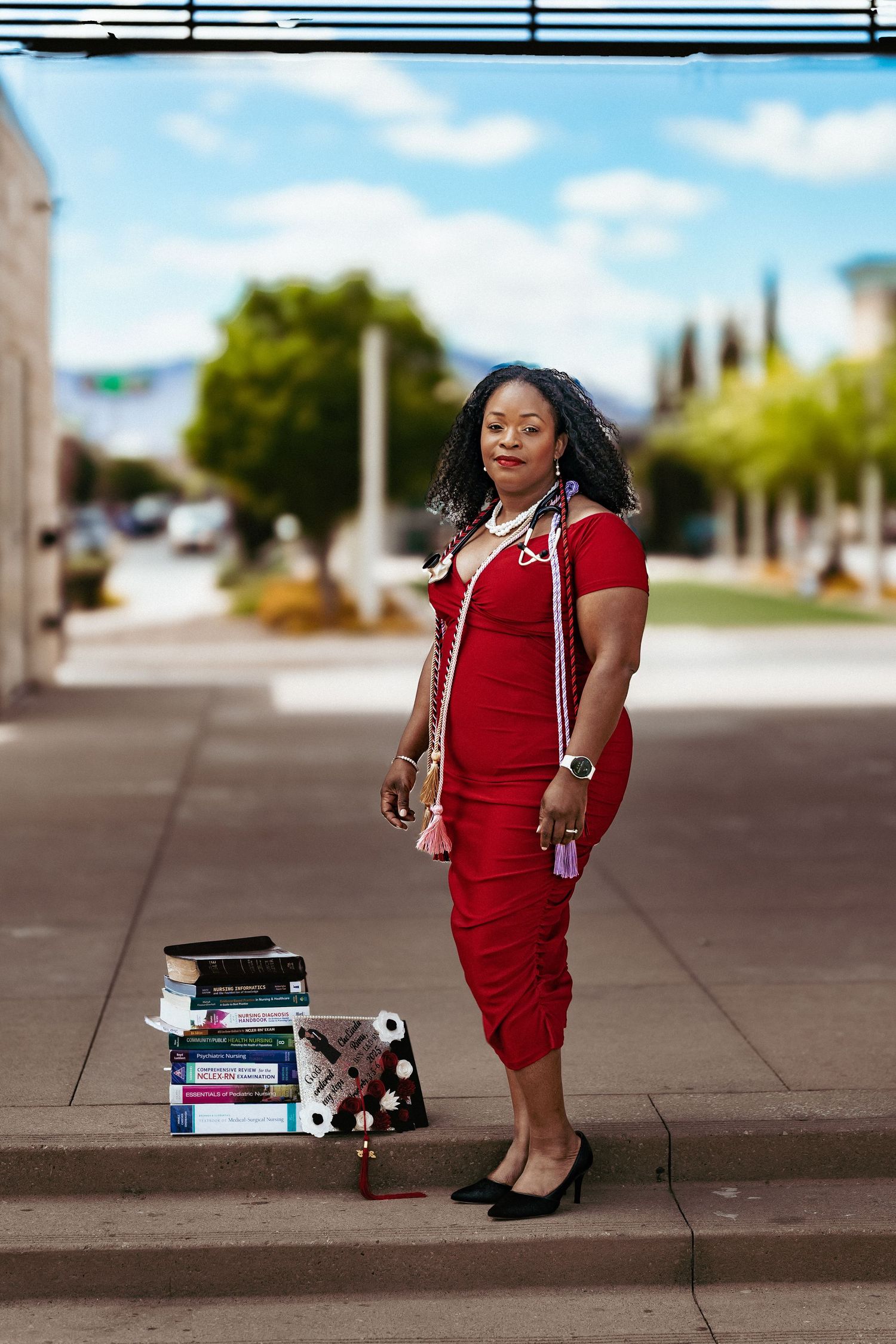 A person in a red dress sits on concrete steps with textbooks scattered around them in an outdoor setting.