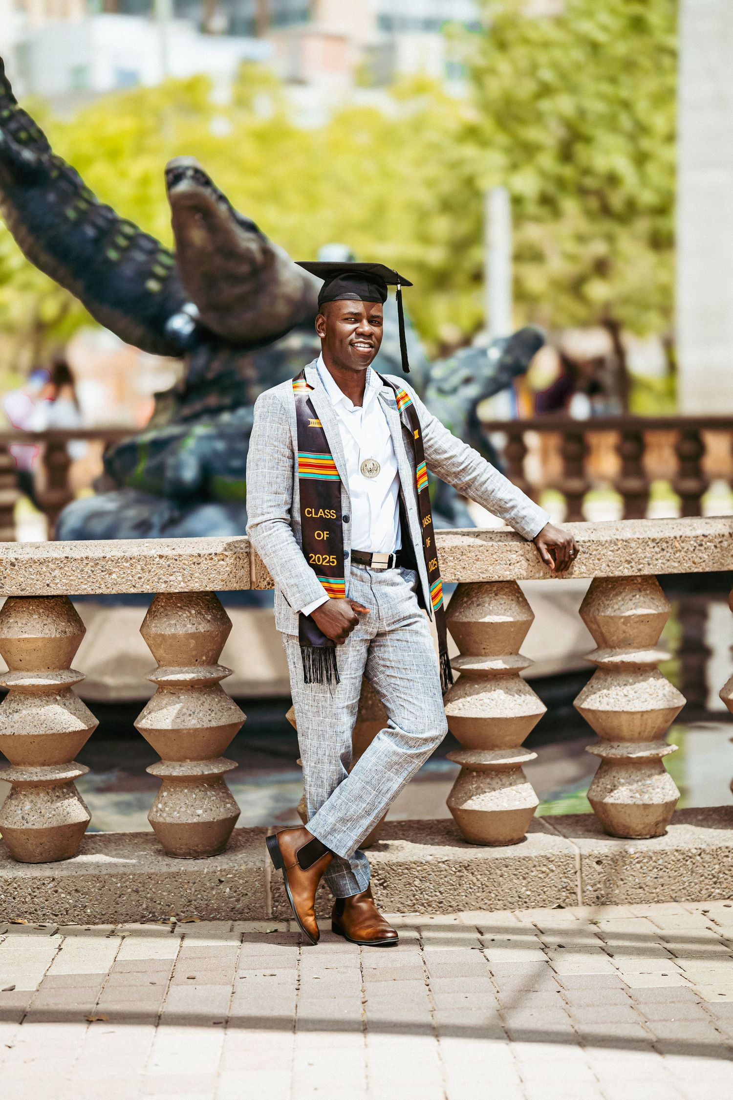 Graduate in white suit and gold stole poses on stone steps during outdoor graduation photoshoot.