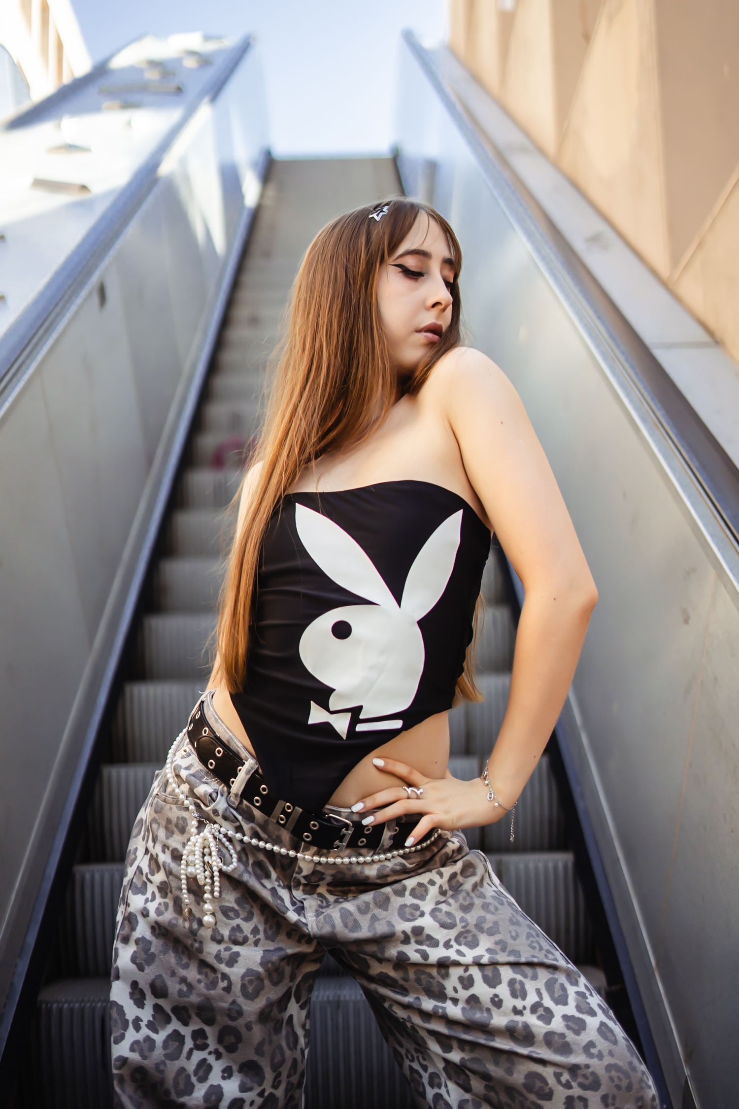 Woman in black top and leopard print pants poses on escalator steps in artistic fashion photo series.