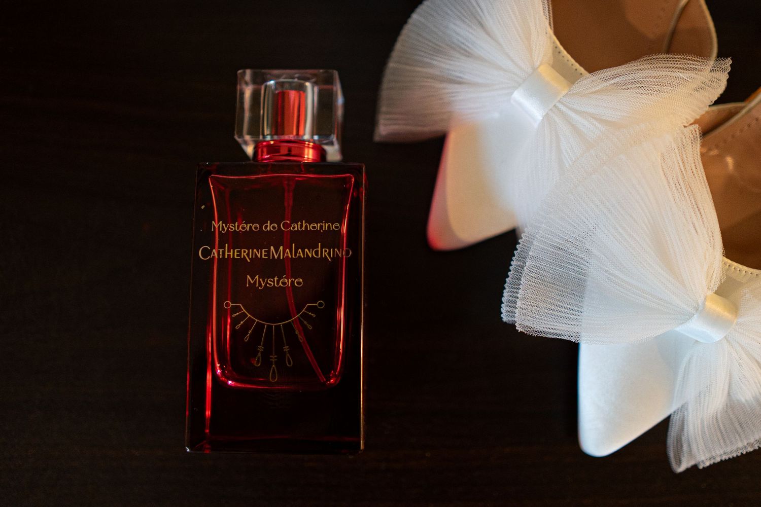 A red perfume bottle with white tulle fabric creates an elegant product photography composition against a dark background.