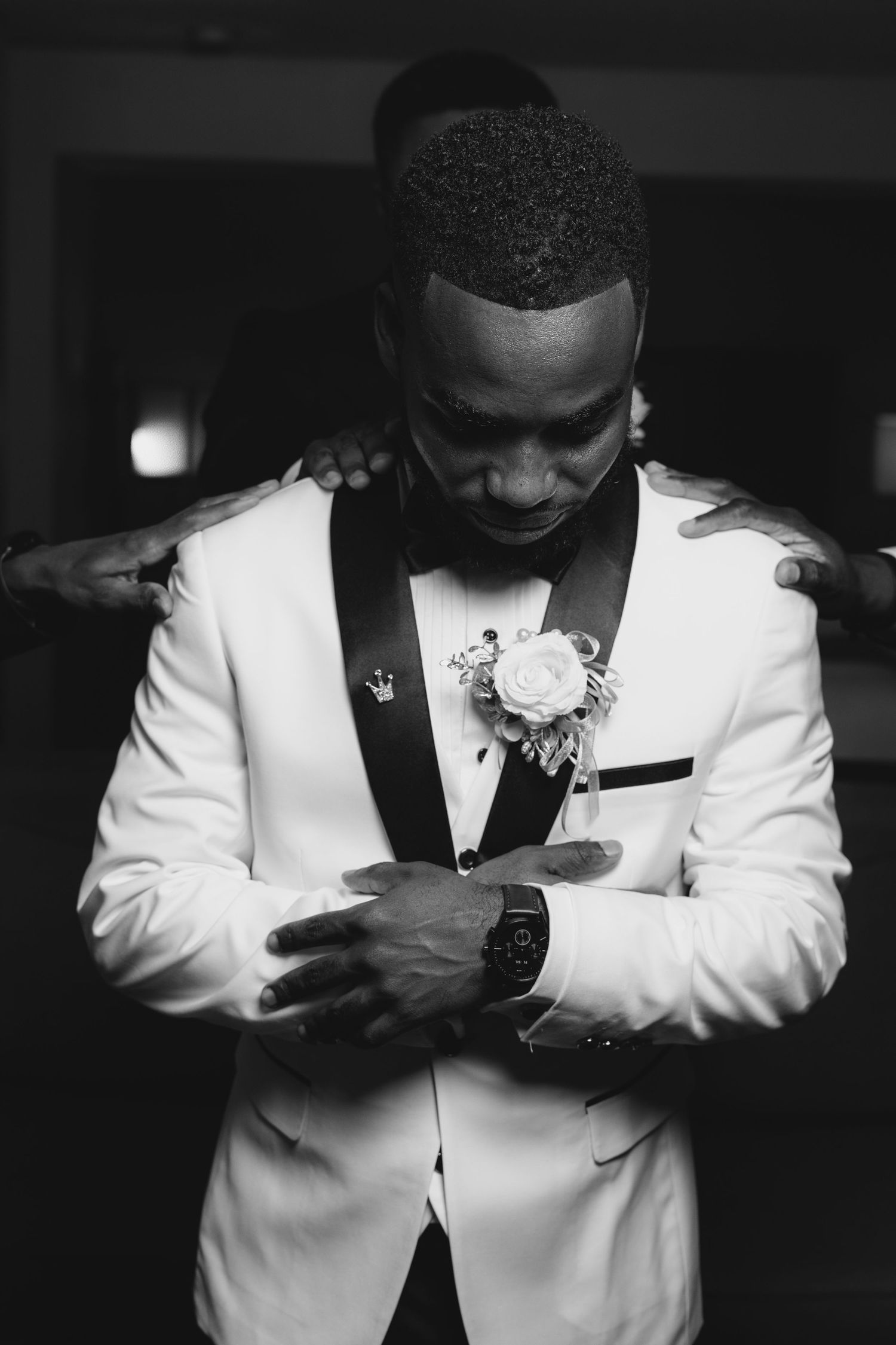 Stylish black and white photo series showing details of a groom adjusting his white tuxedo jacket.