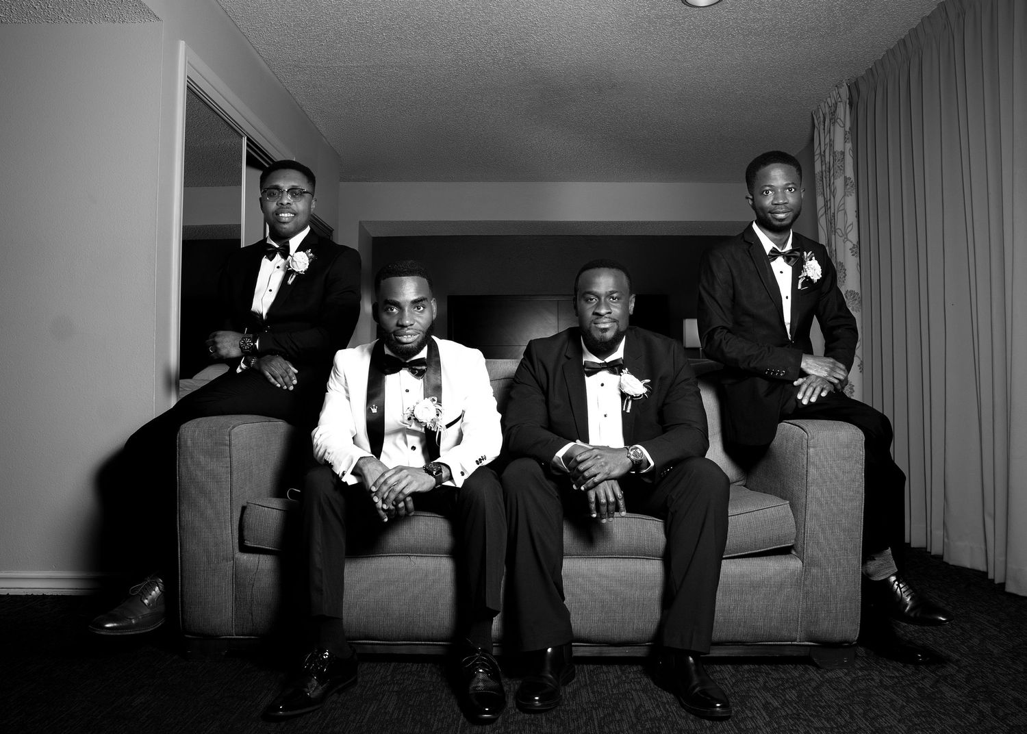 Several people in formal wear sit on a couch in a black and white photograph.