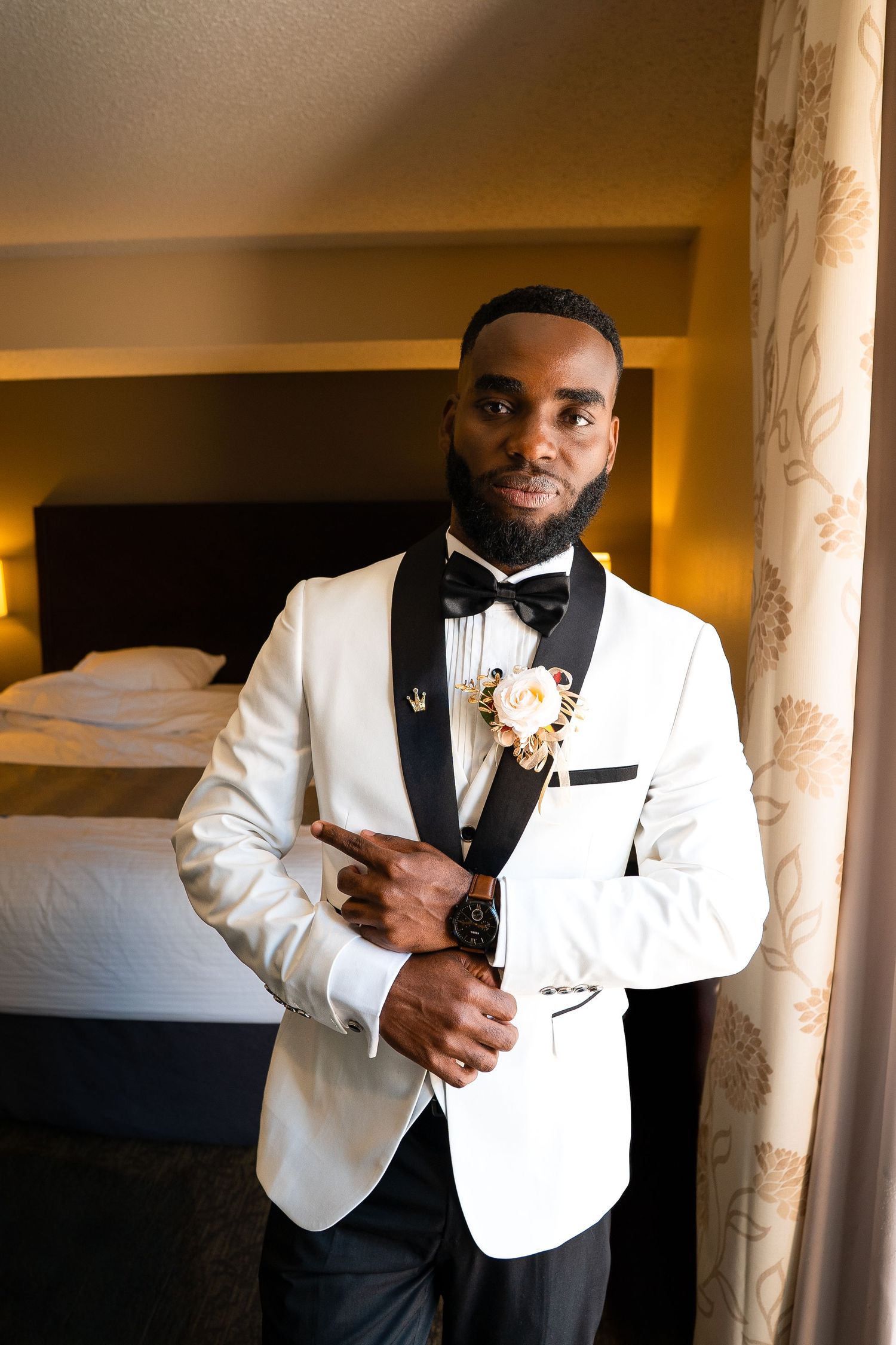 Wedding preparation photos showing elegant white tuxedo and black bow tie in warm indoor lighting.