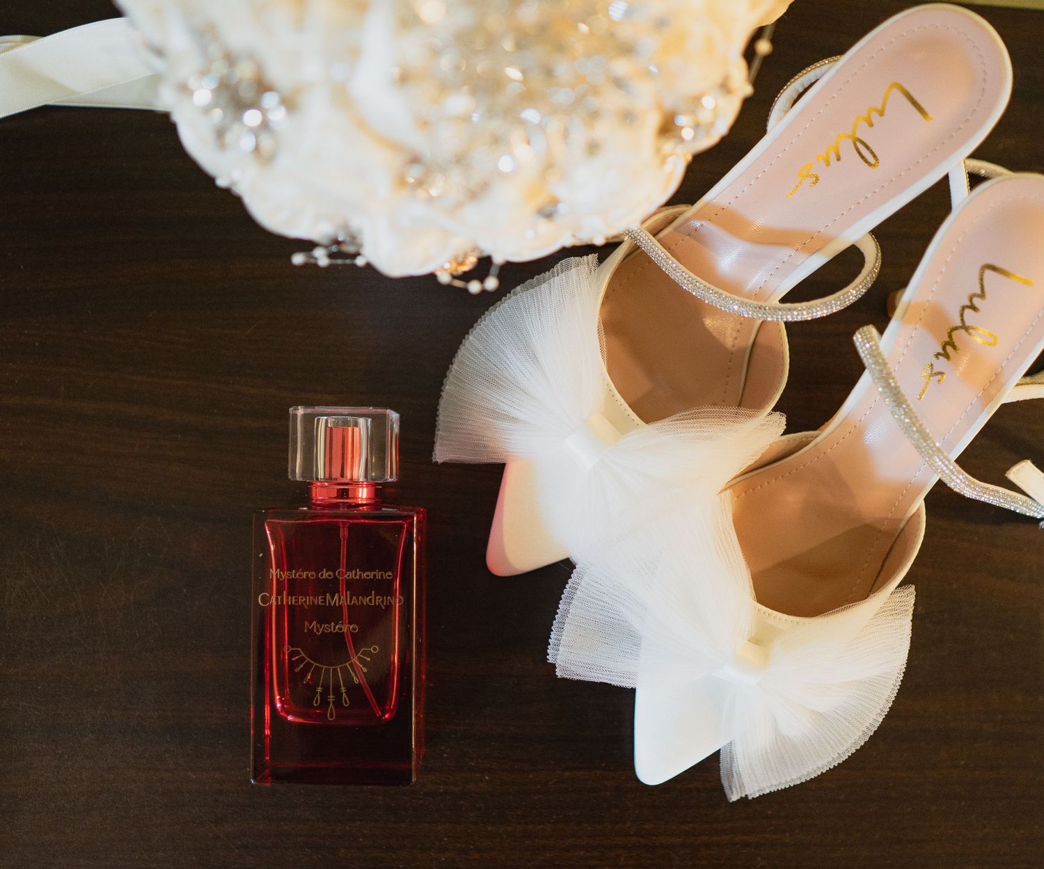 A delicate arrangement of white orchids next to a red perfume bottle on a dark wooden surface.