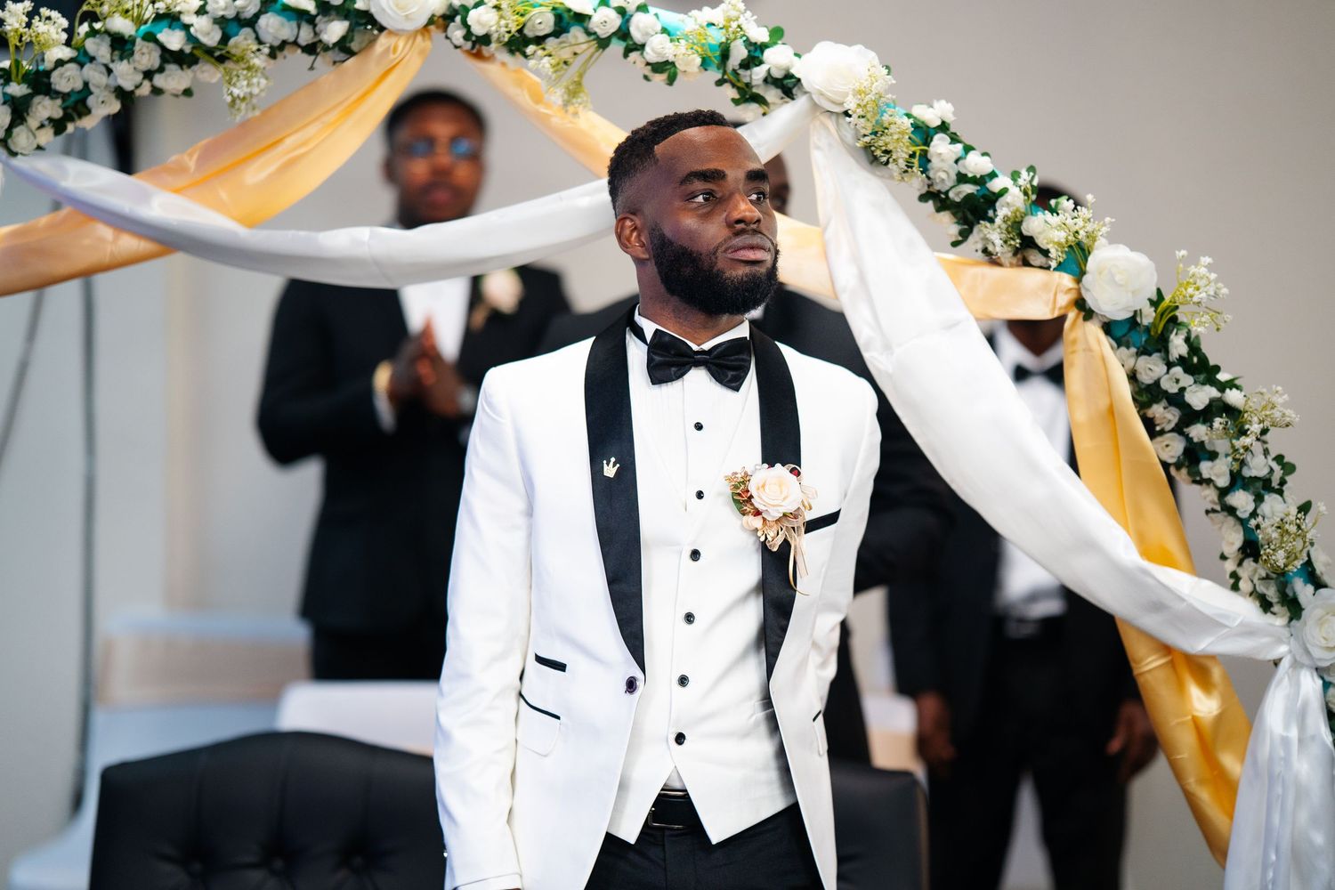 Elegant wedding ceremony setup with white and green floral arch and gold drapery indoors.