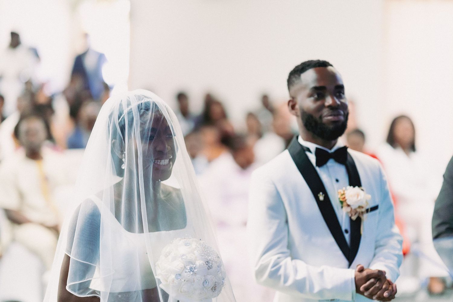 Wedding ceremony guests seated in white chairs during an indoor celebration.