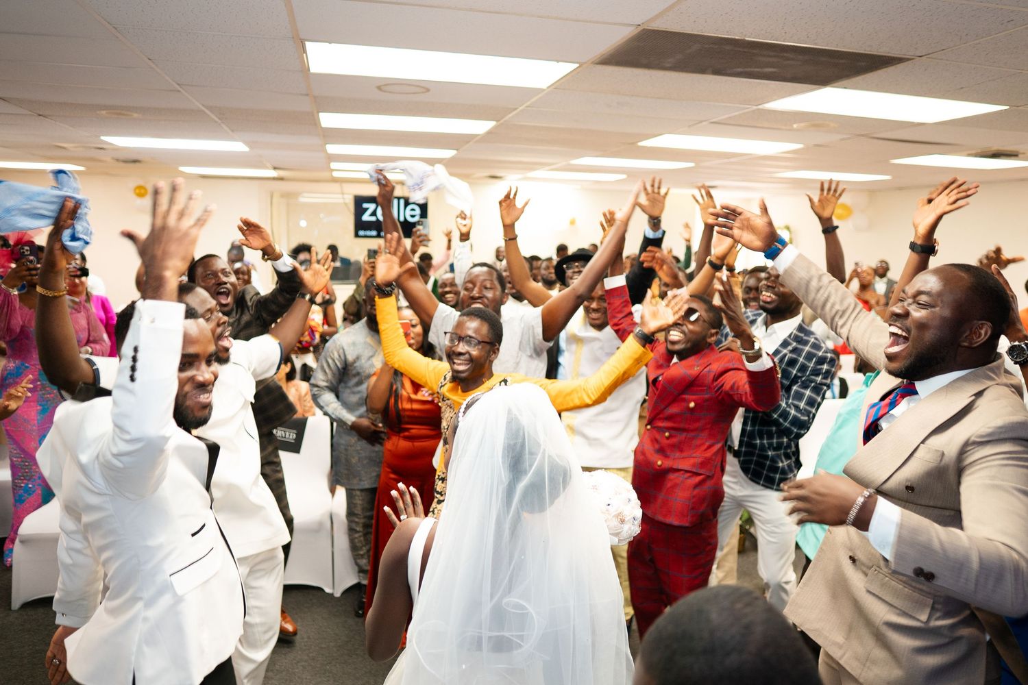 A group of people raise their hands in celebration during what appears to be a joyous gathering in an office setting.