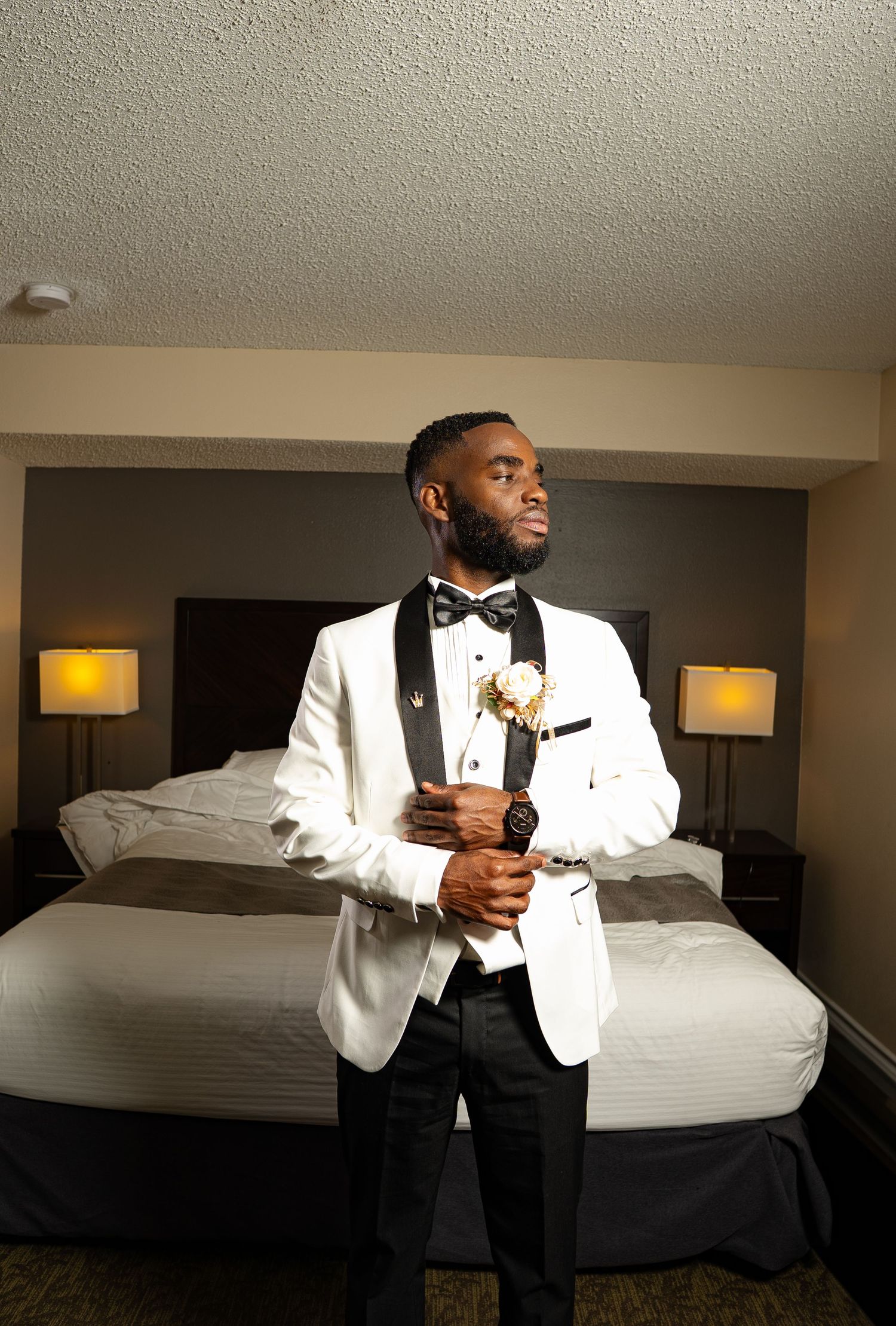A person in a white tuxedo jacket and black bow tie poses in different positions in a hotel room setting.