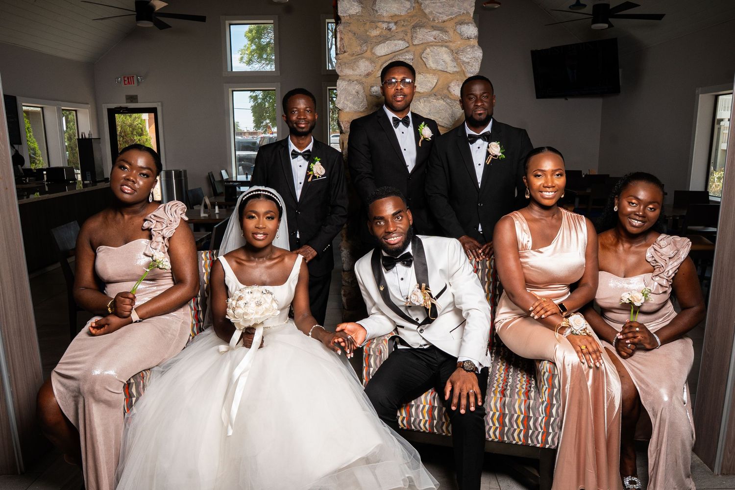 Wedding party relaxes indoors with bridesmaids in light colored dresses seated on elegant furniture.