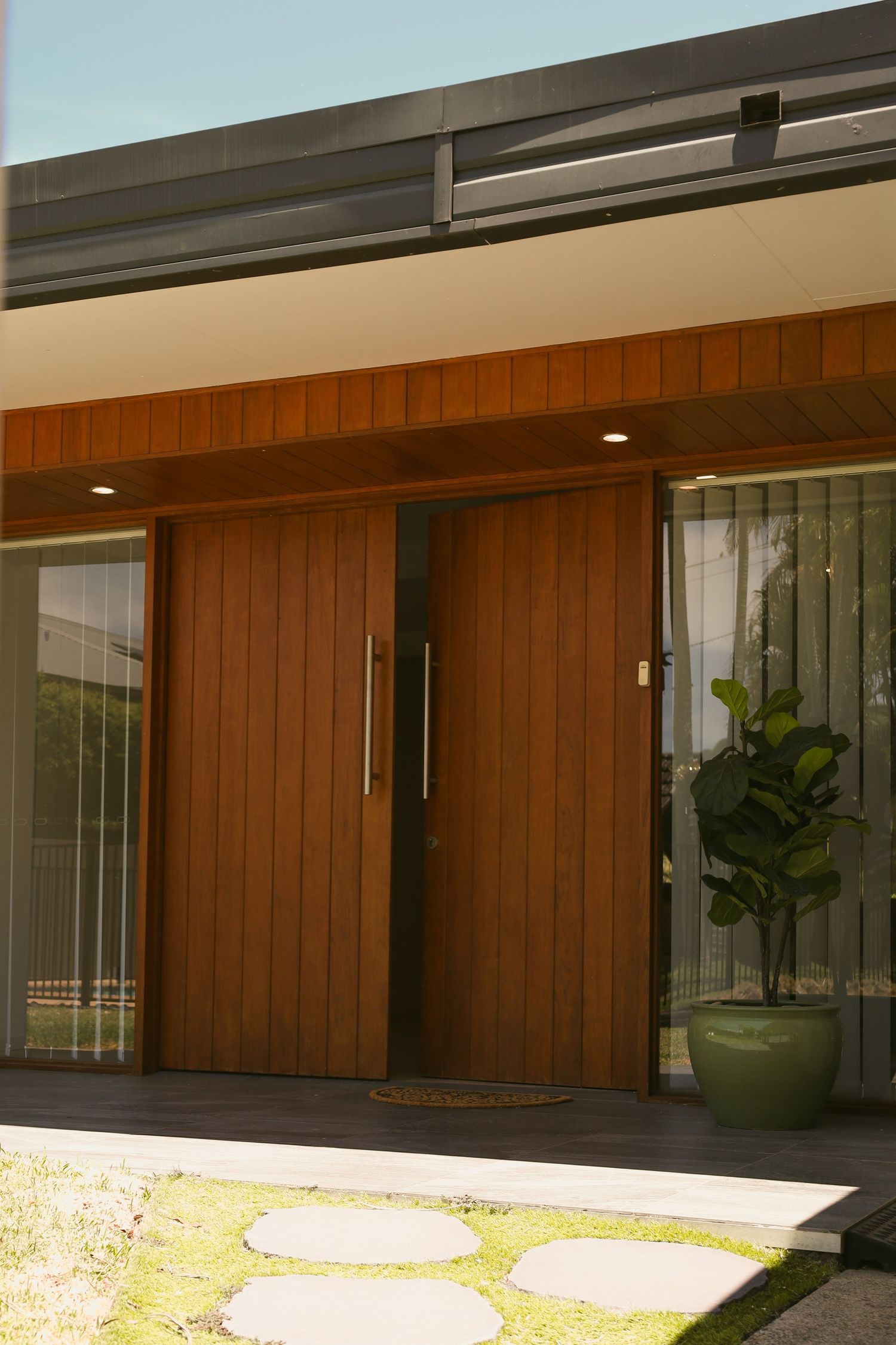Modern home exterior features sleek wood paneling, large glass windows, and minimalist landscaping with potted plants.