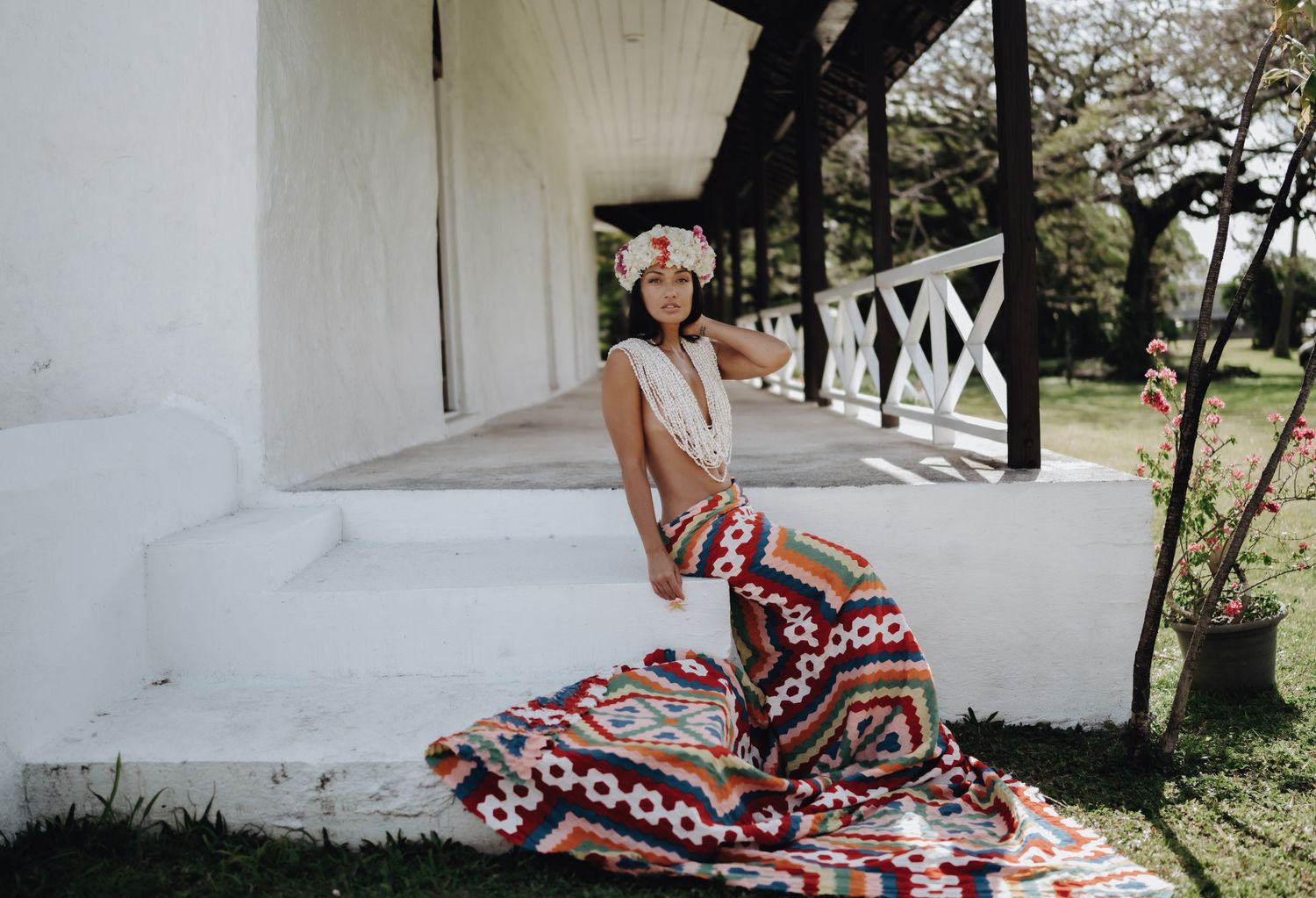 Woman in red and white patterned dress lounges gracefully on white porch steps in outdoor setting.